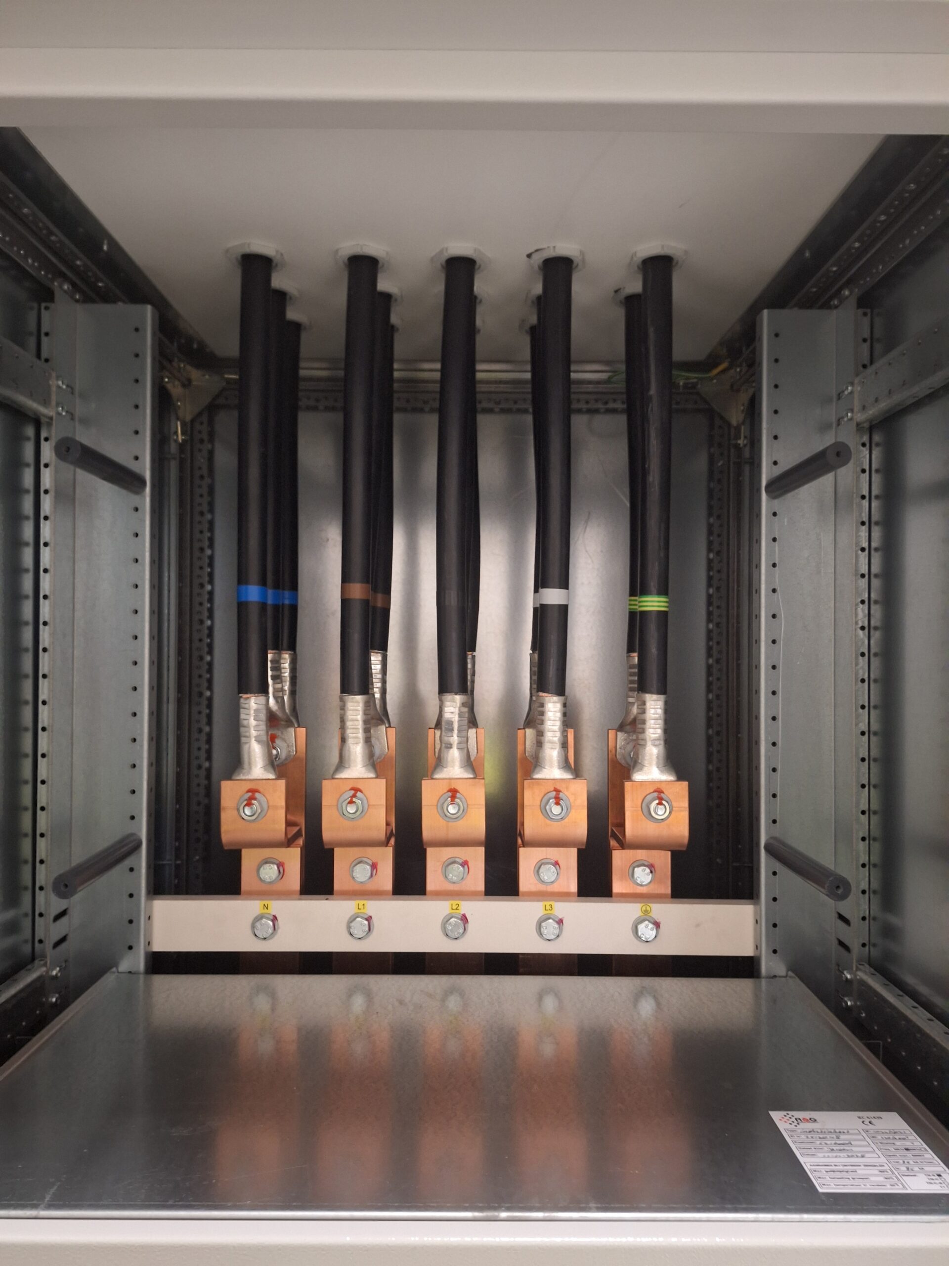 Vijf dikke elektrische kabels aangesloten op koperen klemmen in een metalen elektrisch paneel.