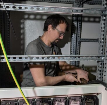 marco uitbreiden station Een man werkt in een open elektriciteitskast, hanteert bedrading en componenten met verschillende kabels en stroomonderbrekers zichtbaar.